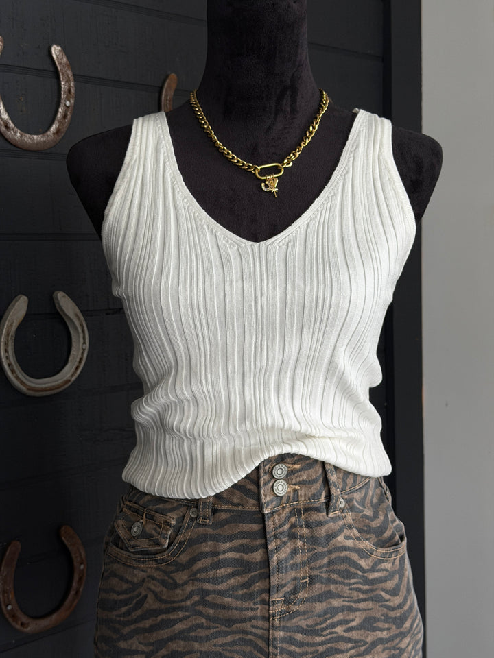 Mannequin wearing a white ribbed tank top and zebra print pants with a gold necklace against a dark background.