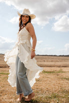 Woman in a white ruffled boho dress, blue jeans, and cowboy hat standing in a field