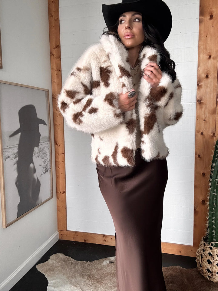 Woman wearing a cow print fur coat and black hat indoors.