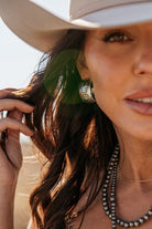 Woman wearing western silver hoop earrings, layered beaded necklaces, and cowboy hat outdoors