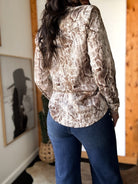 Woman wearing snakeskin print western blouse and blue denim flare jeans in rustic room