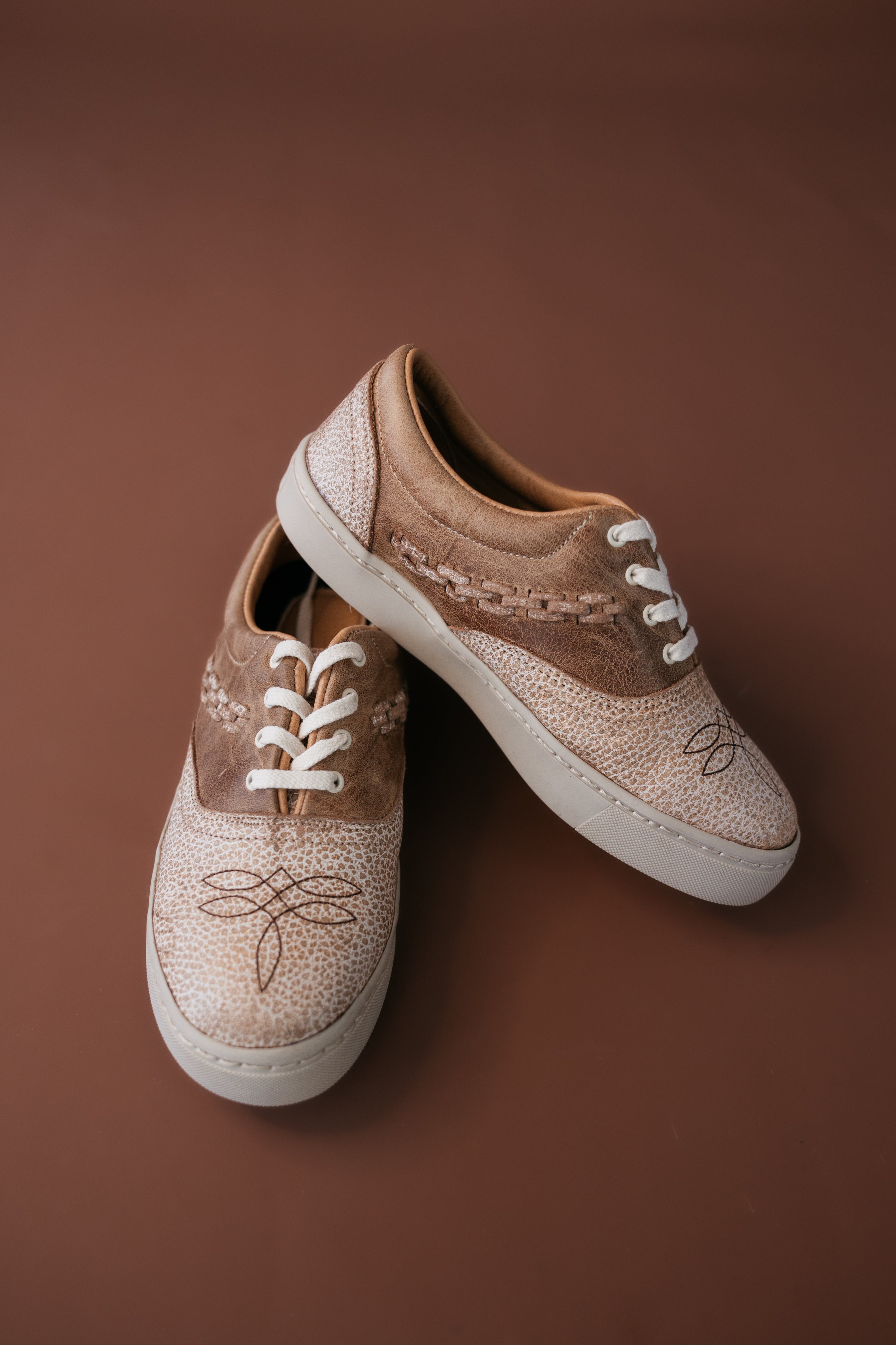 Western boho leather sneakers with white laces and stitched detailing on brown background