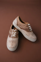 Western boho leather sneakers with white laces and stitched detailing on brown background
