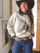 Woman in western boho outfit with cowboy hat, horse graphic sweatshirt, denim shirt, and turquoise belt.