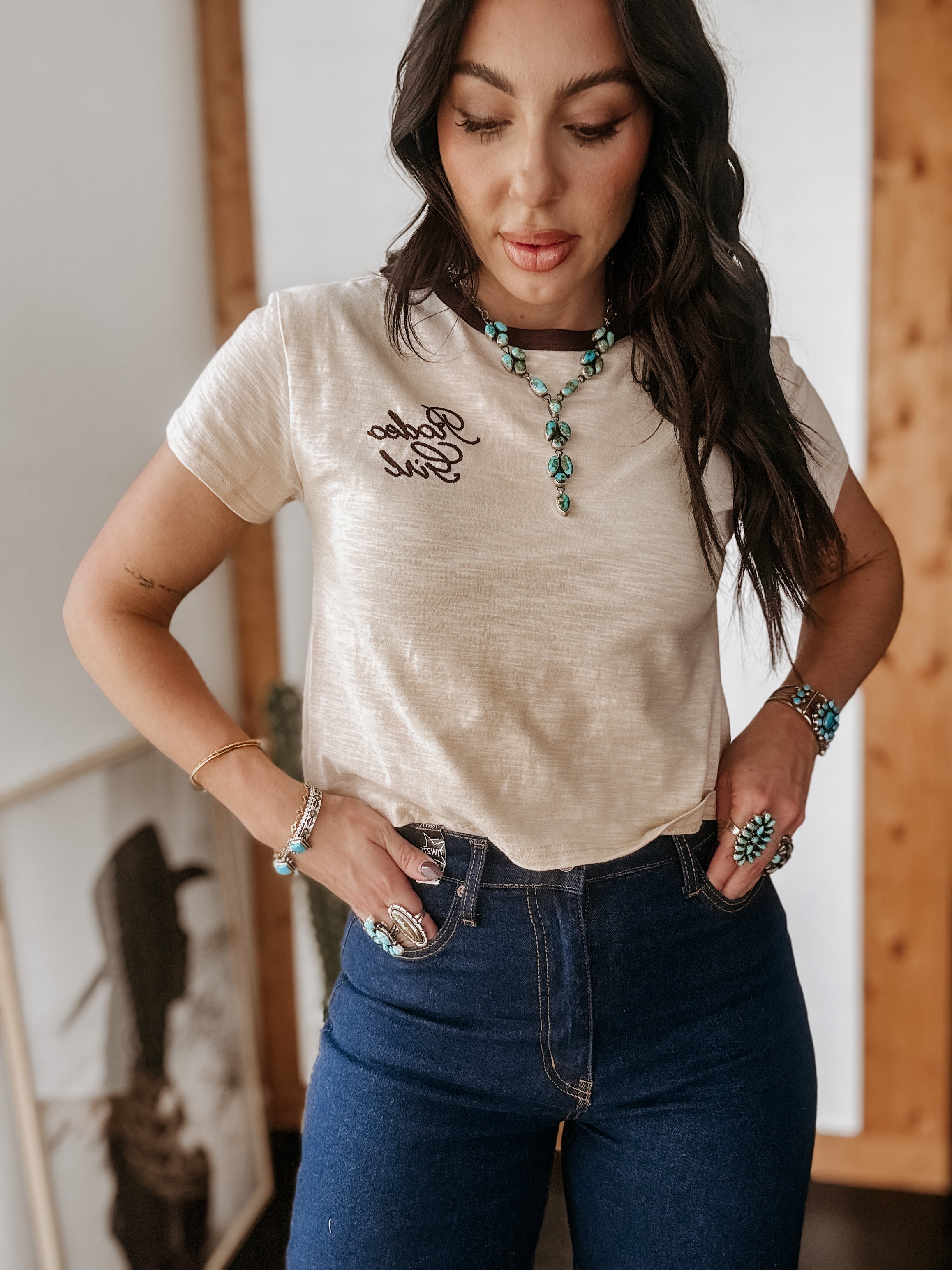 Woman in western boho outfit wearing 'Rodeo Girl' t-shirt, turquoise jewelry, and high-waisted jeans