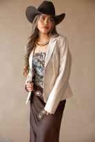Woman in western boho outfit with cowboy hat, cream blazer, graphic tube top, brown skirt, and concho belt