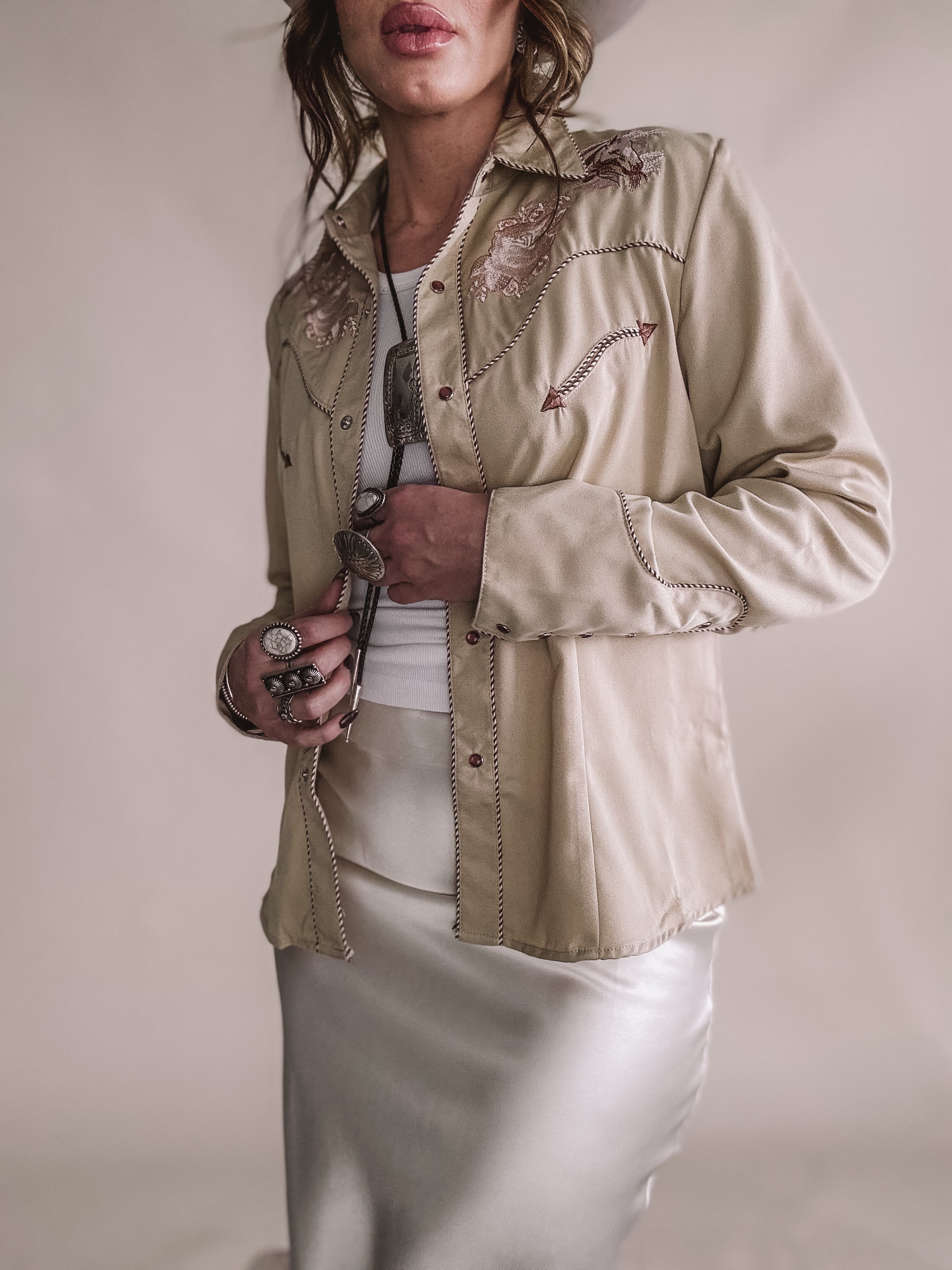 Woman in embroidered western shirt, satin skirt, cowgirl hat, and boho jewelry