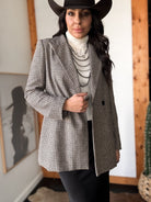 Woman in western boho outfit with houndstooth blazer, white turtleneck, black hat, layered necklaces