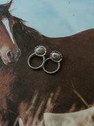 Western concho stud earrings with twisted rope design on horse print background