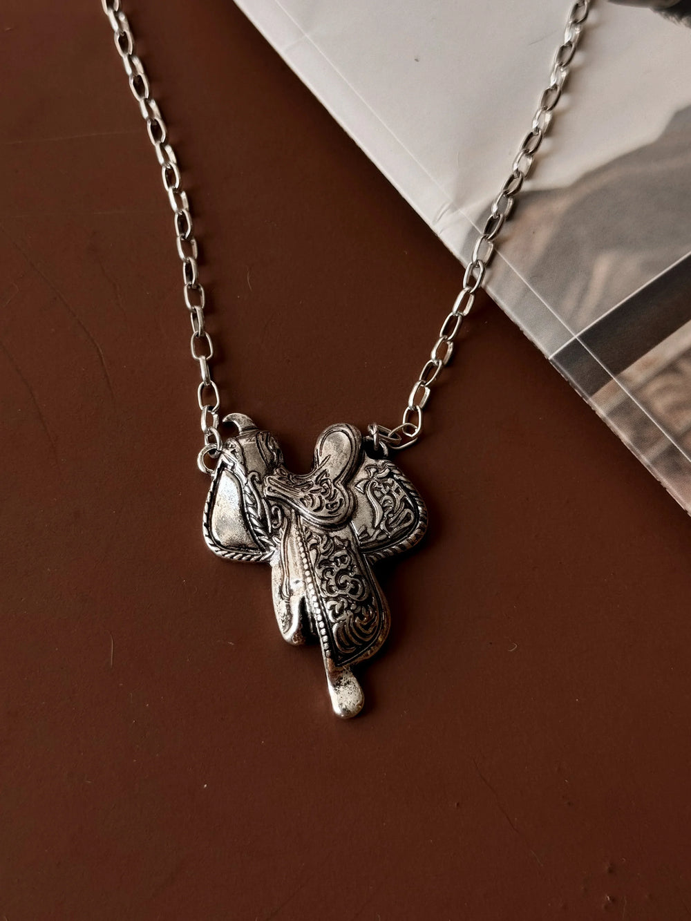 Silver necklace with a detailed pendant on a brown surface