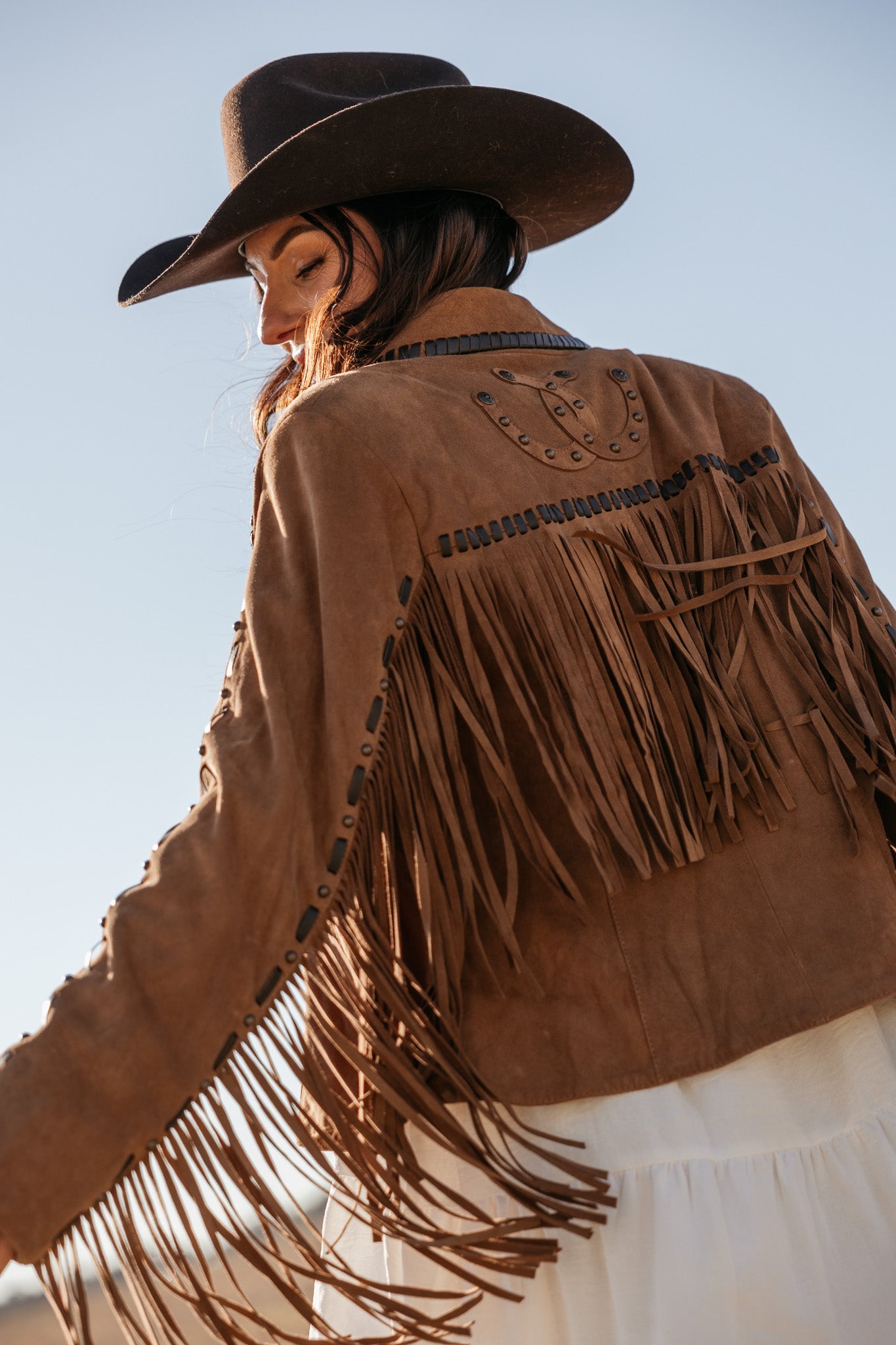 Woman in brown suede fringe western jacket and black cowboy hat, boho cowgirl style