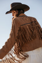 Woman in brown suede fringe western jacket and black cowboy hat, boho cowgirl style