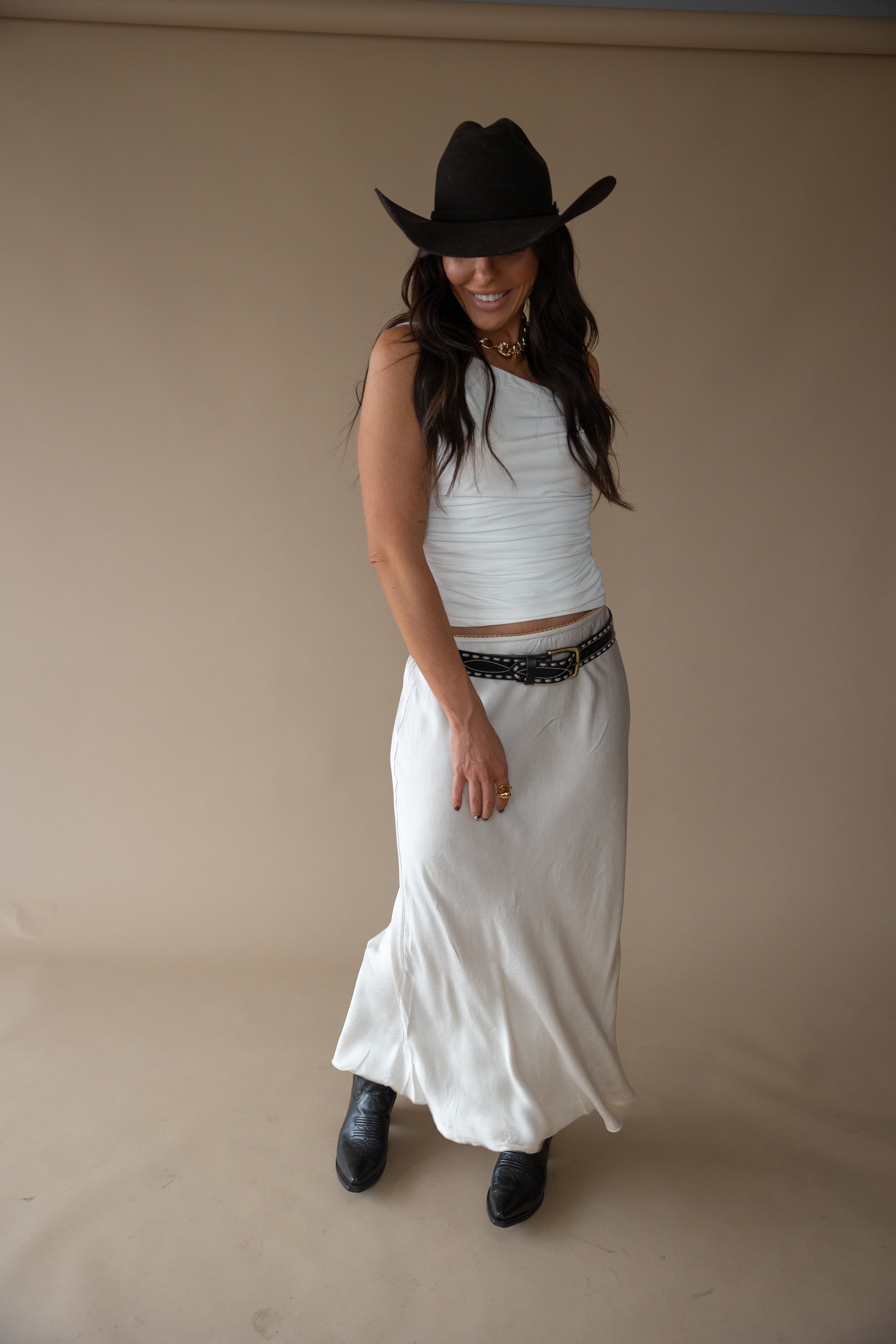 Woman in western boho outfit with cowboy hat, white tank top, long skirt, belt, and boots