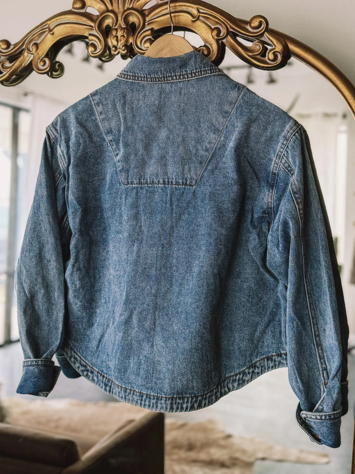 Vintage blue denim jacket with western yoke detail hanging on ornate mirror