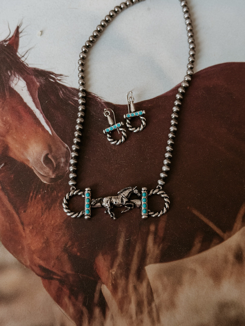 Western silver horse necklace with turquoise accents and matching earrings on a horse background