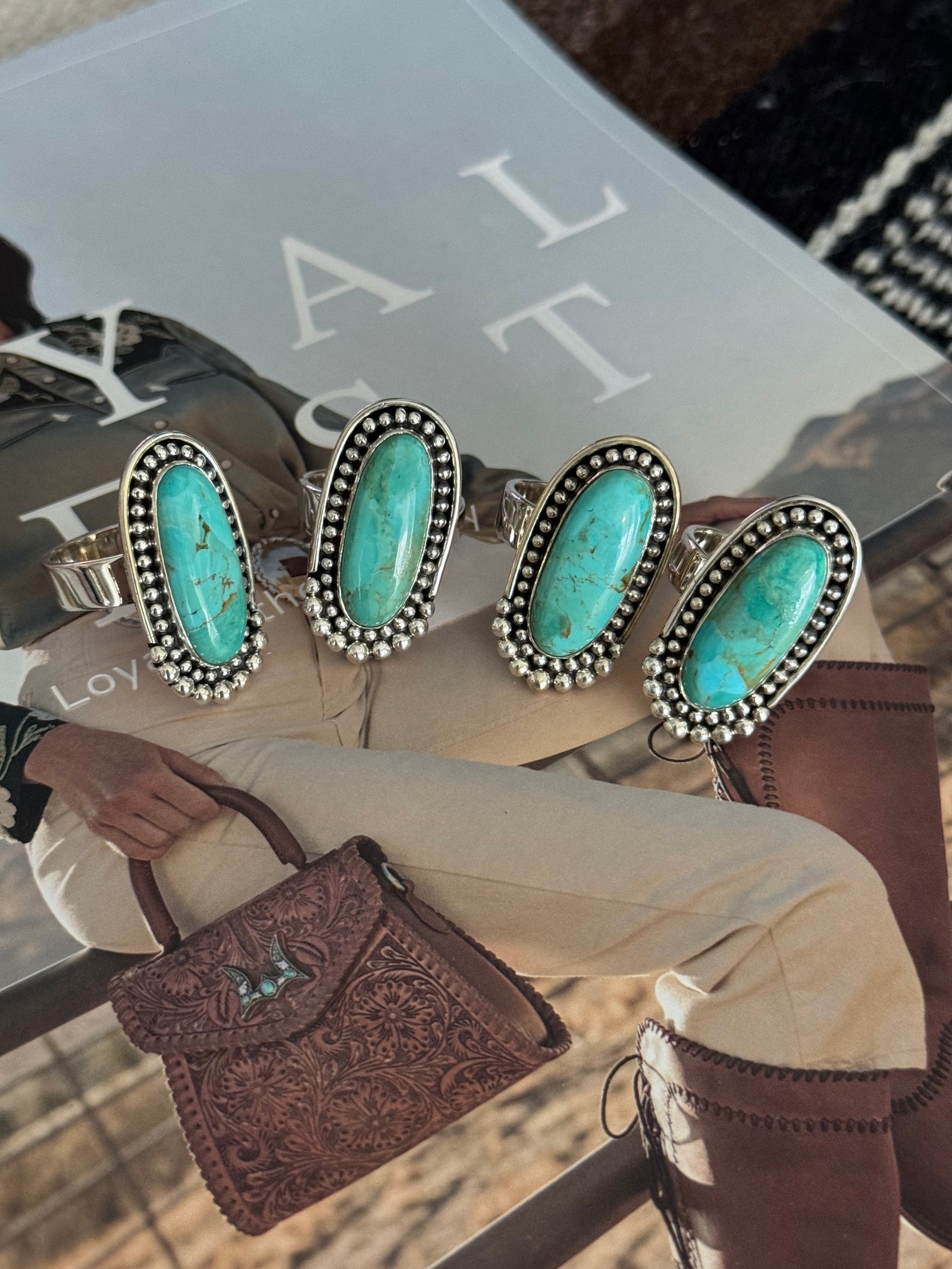 A collection of four adjustable sterling silver rings with large turquoise stones displayed on a person's finger and hand.