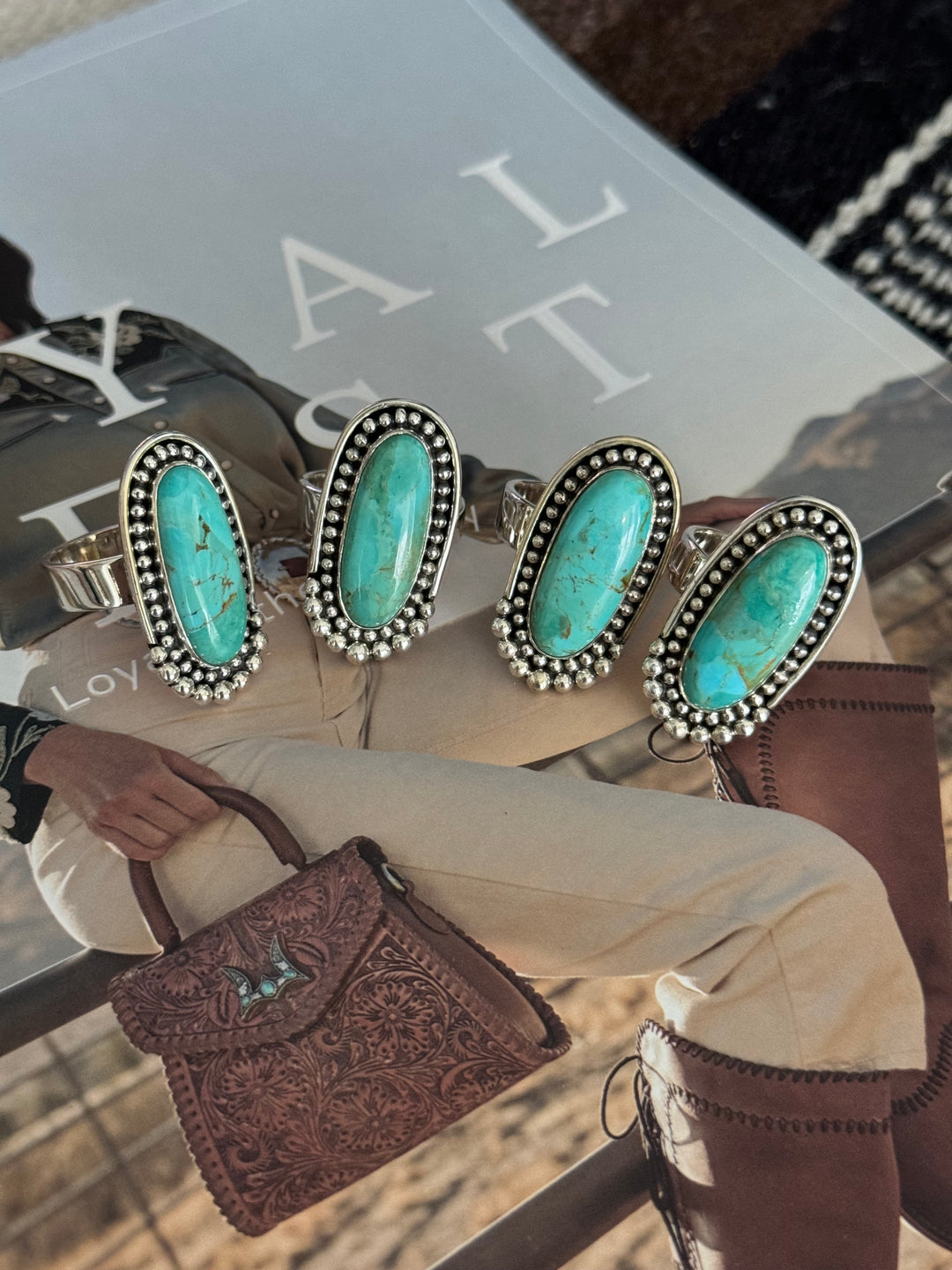 A collection of four adjustable sterling silver rings with large turquoise stones displayed on a person's finger and hand.