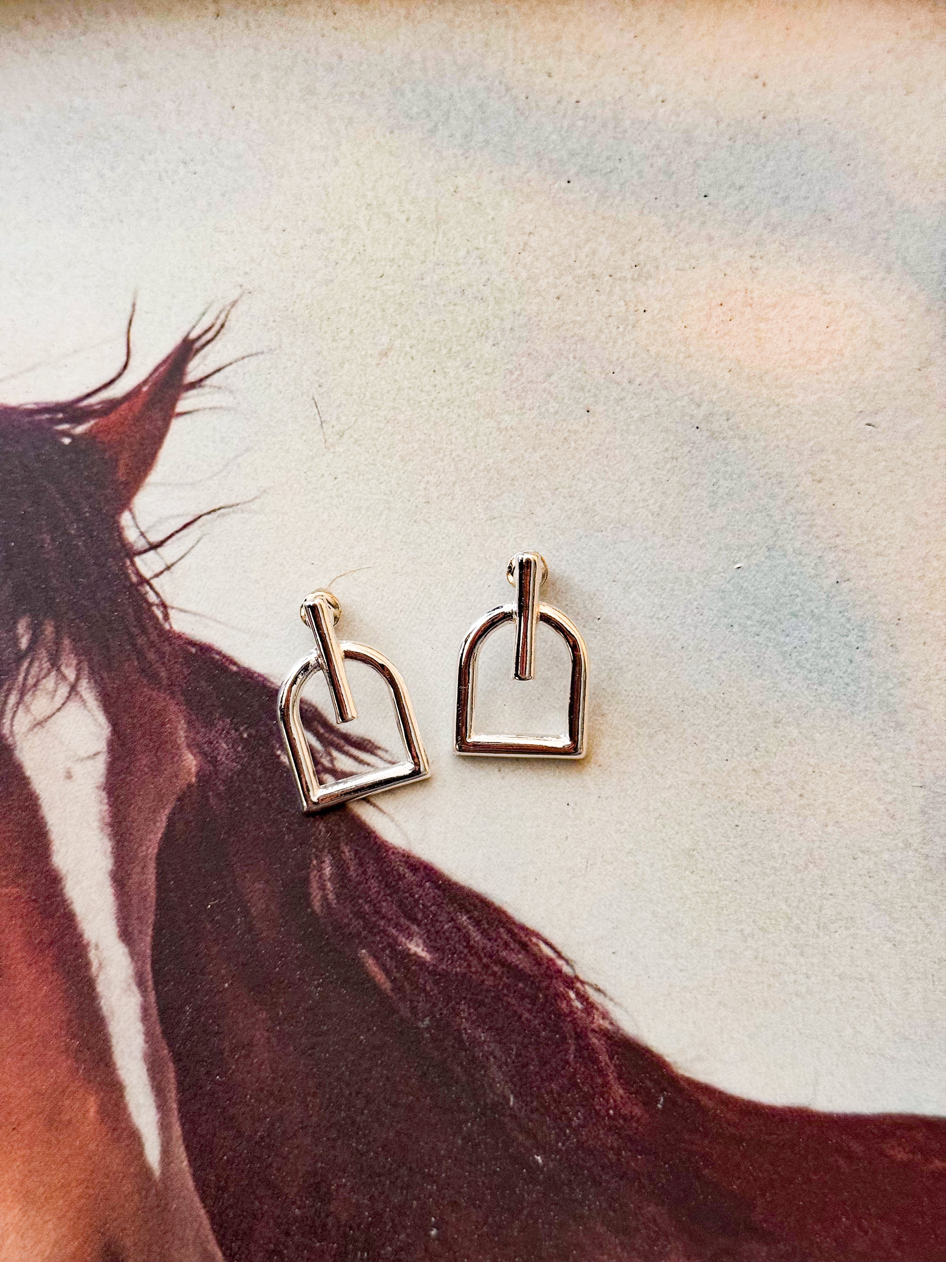 Silver western stirrup earrings on a horse-themed background, boho cowgirl jewelry.