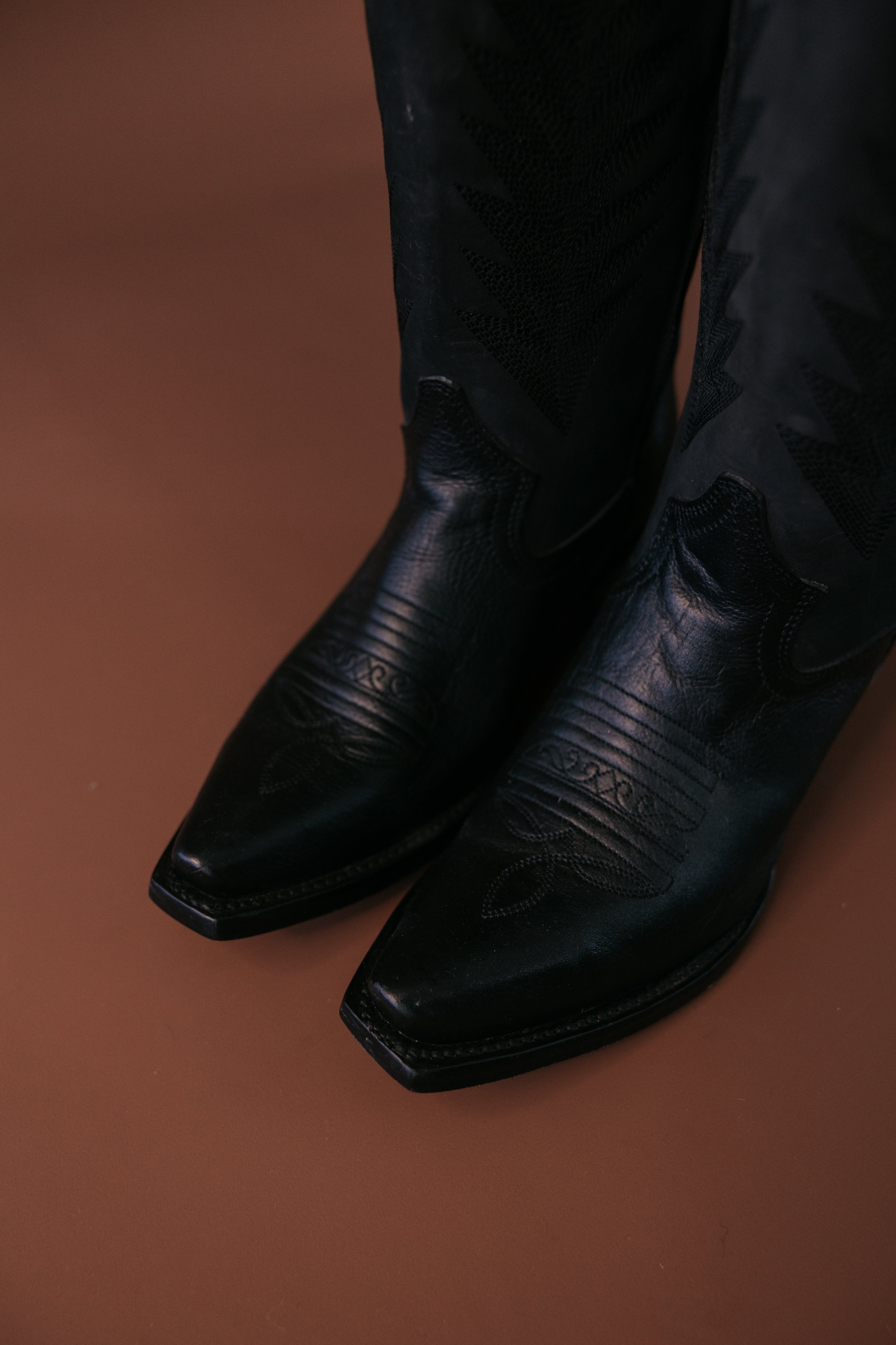 Black leather western cowgirl boots with stitched details on brown background
