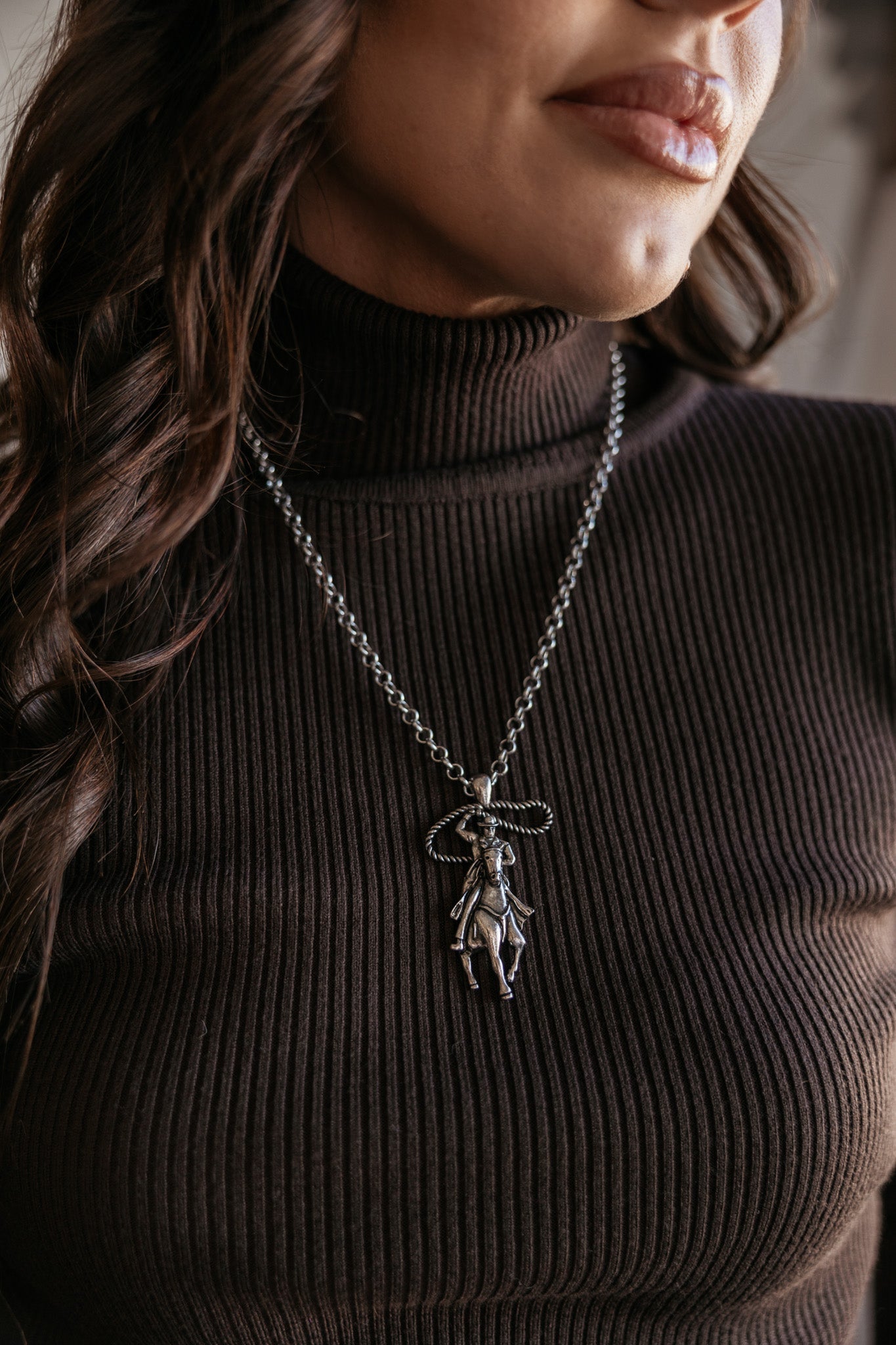 Woman wearing western cowgirl necklace with horse pendant over ribbed brown turtleneck top