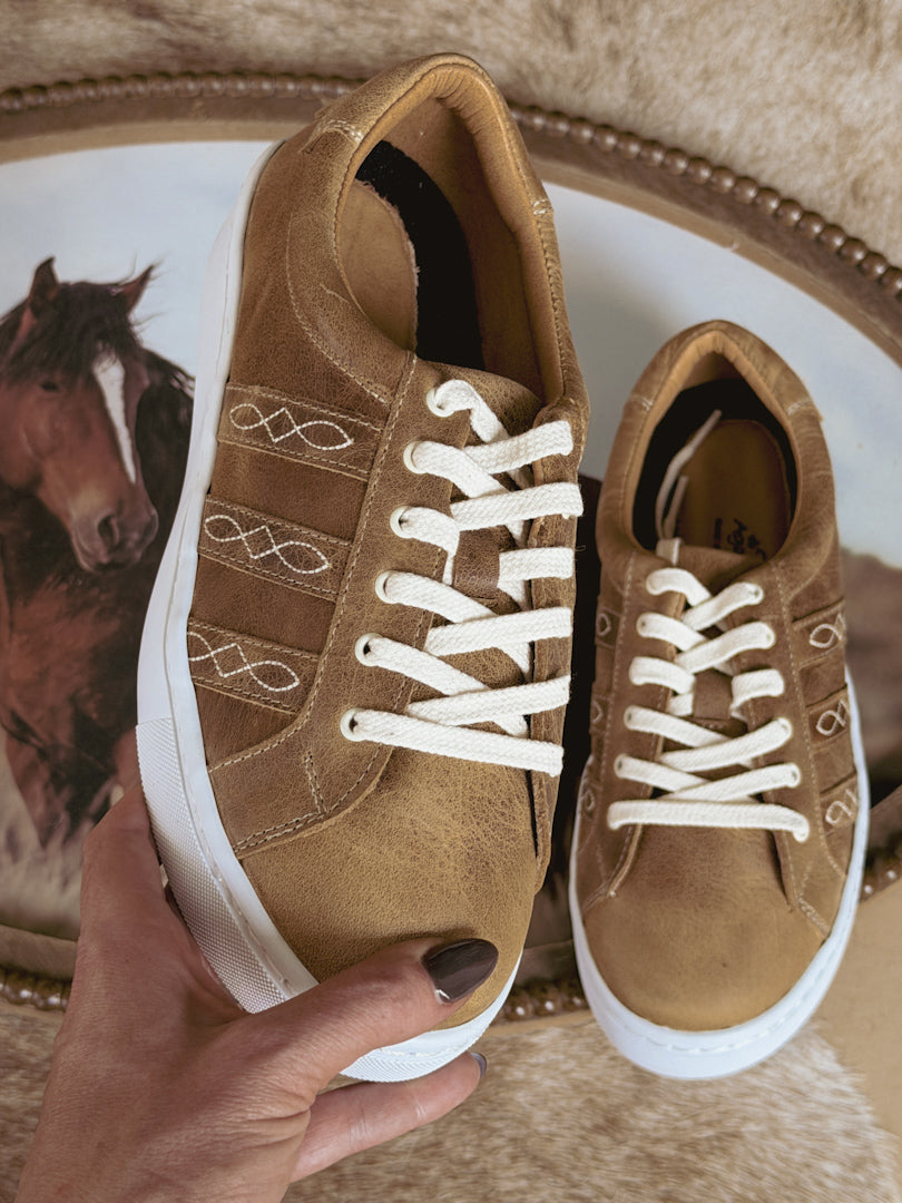 Tan western boho sneakers with white laces, cowhide background, horse decor accent.