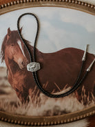 Western braided leather bolo tie with engraved silver slide on horse art background