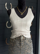 Mannequin wearing a white ribbed tank top and patterned pants with gold jewelry against a dark background.