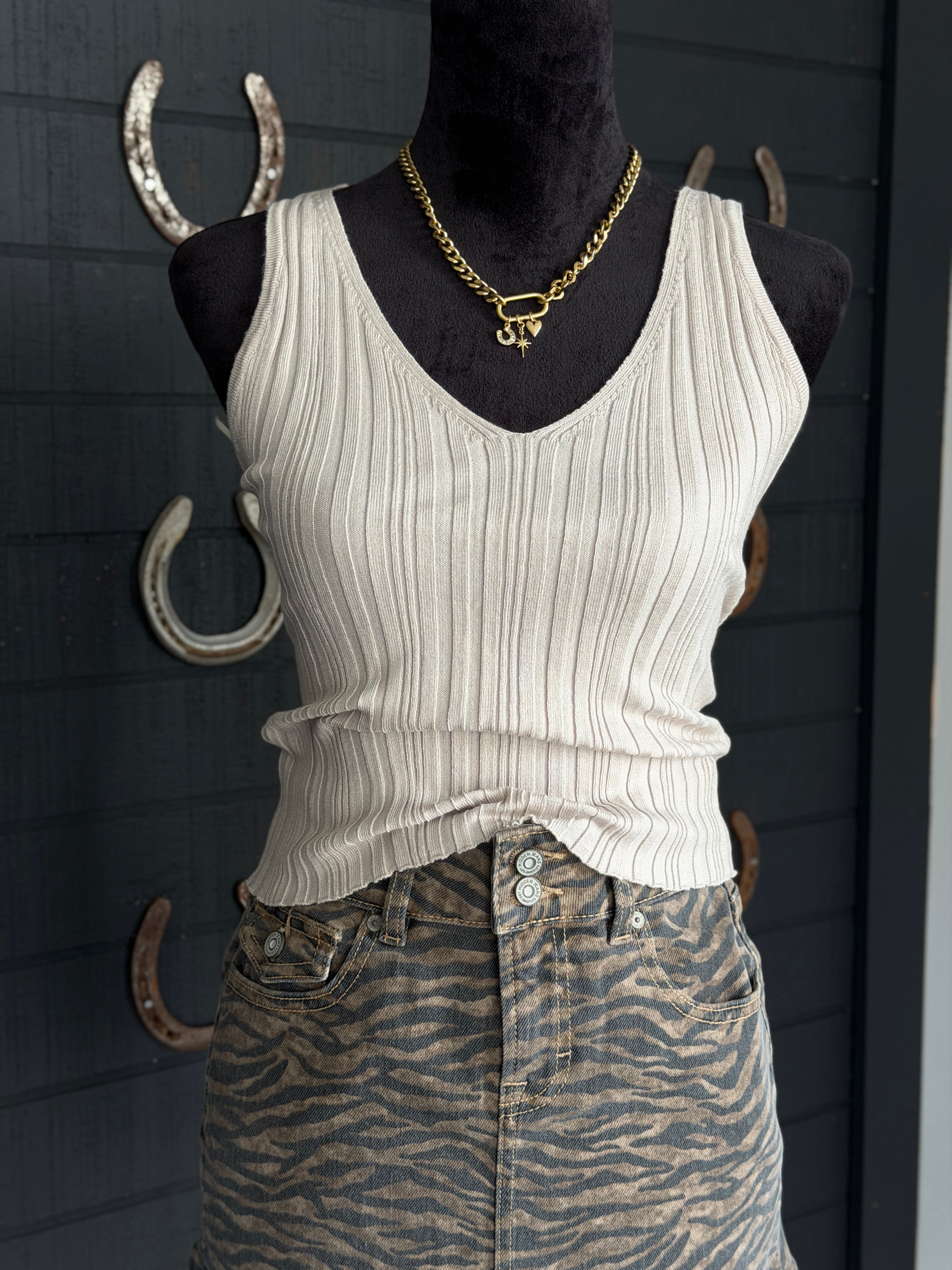 Mannequin wearing a white ribbed tank top and patterned pants with gold jewelry against a dark background.