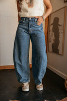 Woman wearing wide leg denim jeans, cream knit crop top, western jewelry, and sneakers