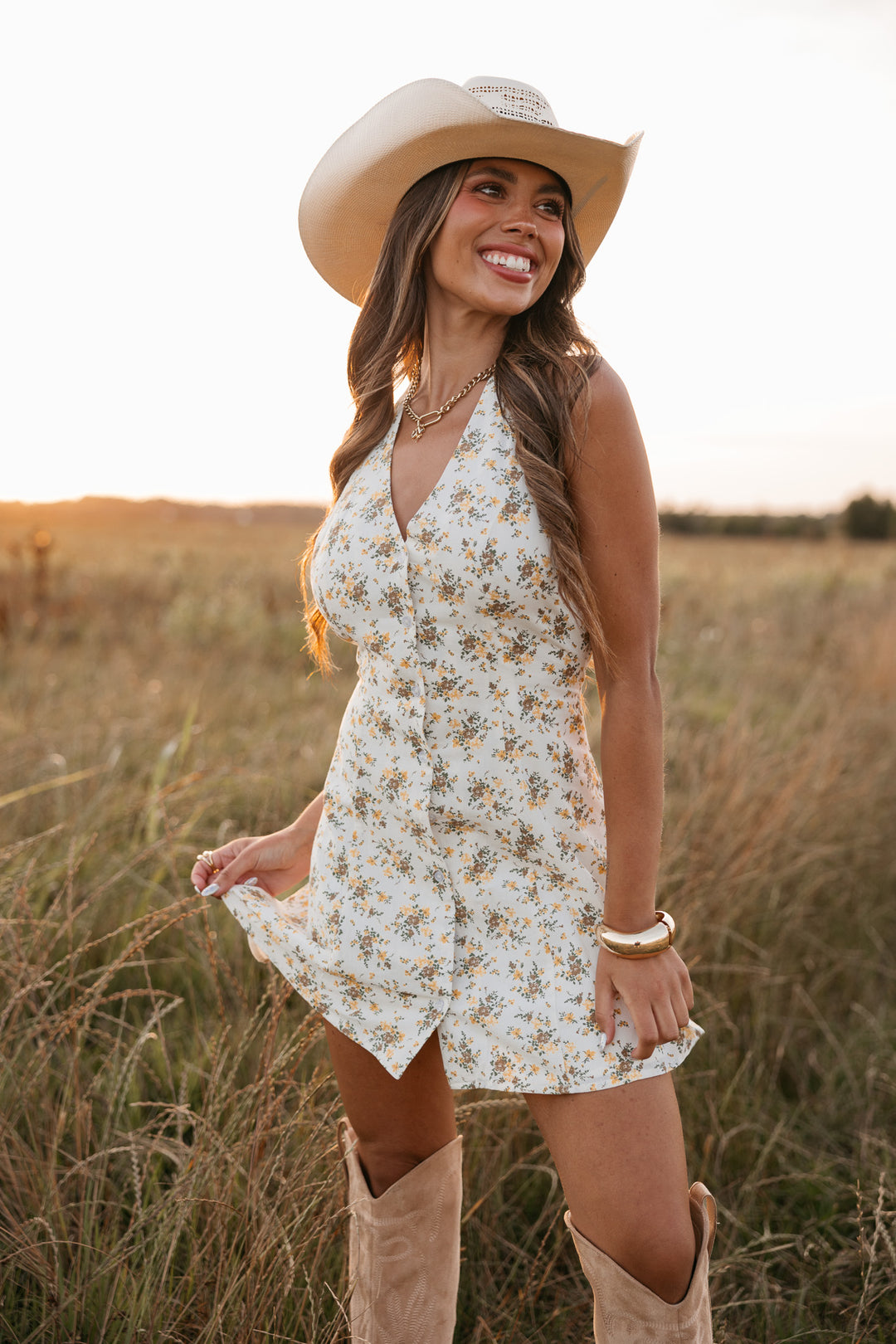 Woman in a floral dress and cowboy hat standing in a field.