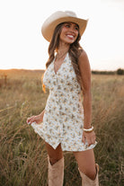 Woman in a floral dress and cowboy hat standing in a field.