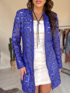 Woman in a blue floral mesh western jacket over a white dress, wearing a bolo tie.
