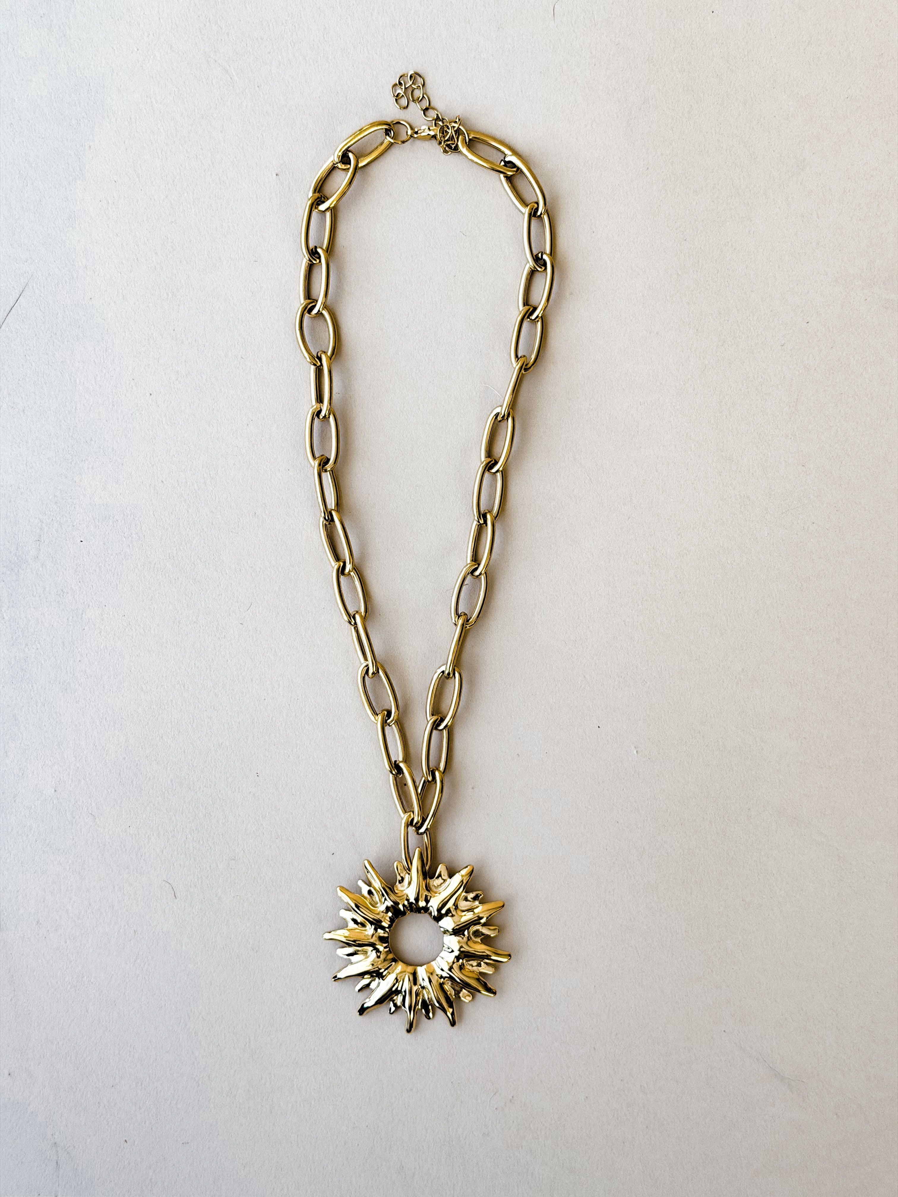 Gold chain necklace with a starburst pendant on a light gray background
