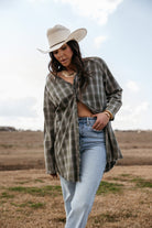Woman in a white cowboy hat, plaid shirt, and light wash jeans in a western field setting