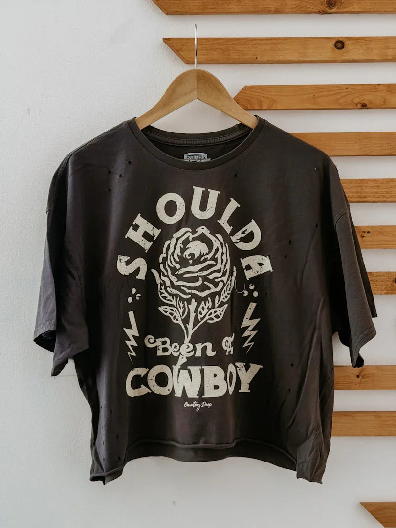 Black t-shirt with white graphic and text on a hanger against a wooden panel background