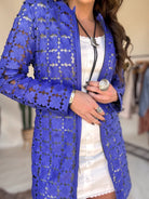 Woman in a white western dress with a bold blue floral mesh jacket, silver jewelry, and bolo tie.