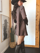 Woman in brown western mini dress, black cowboy hat and boots, standing indoors by cactus