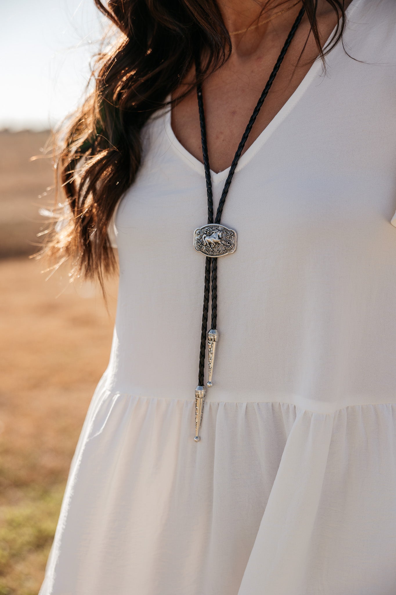 Woman wearing a western bolo tie with engraved silver clasp and white boho dress outdoors