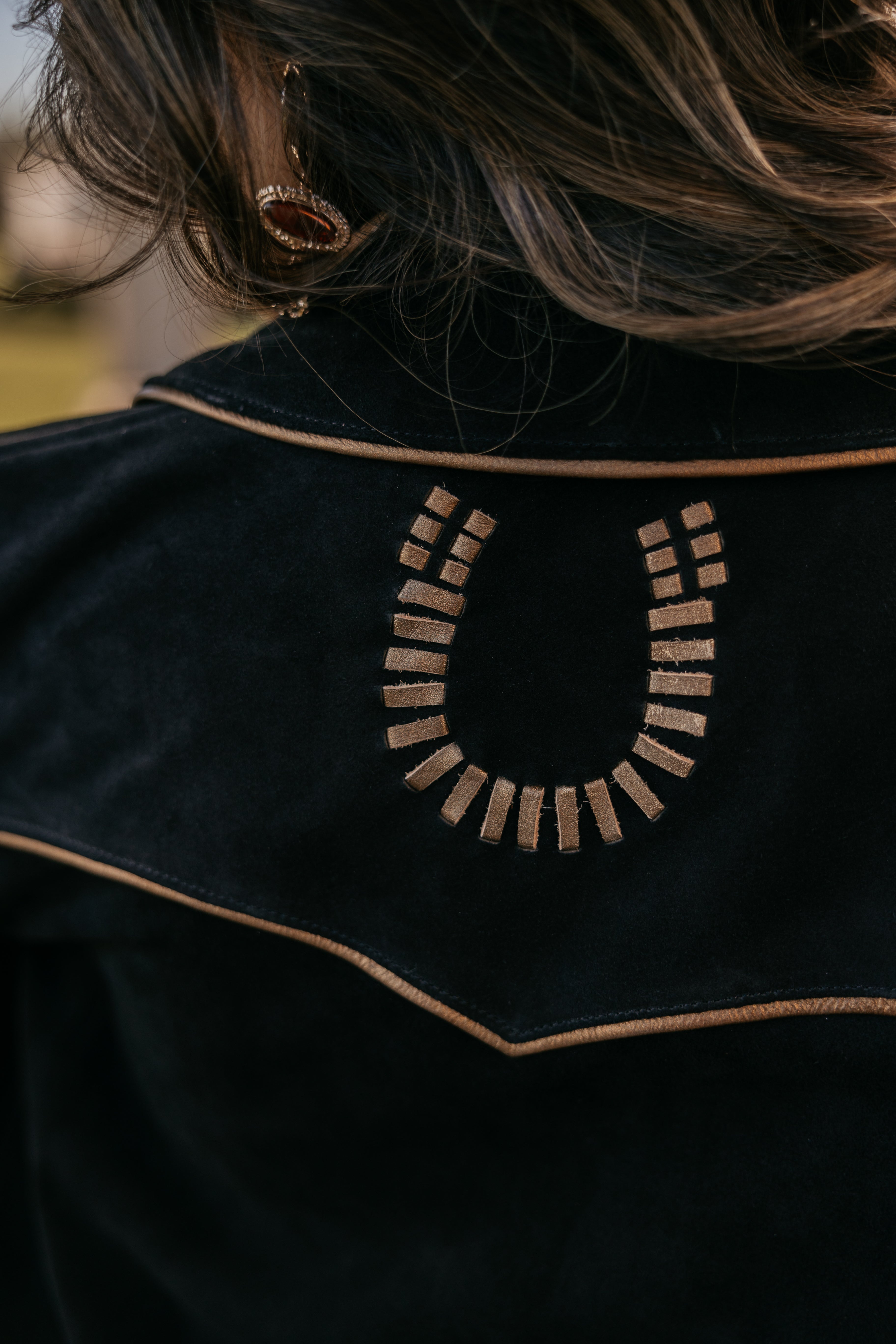 Close-up of western suede jacket with embroidered horseshoe design and brown piping