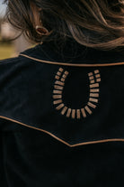 Close-up of western suede jacket with embroidered horseshoe design and brown piping