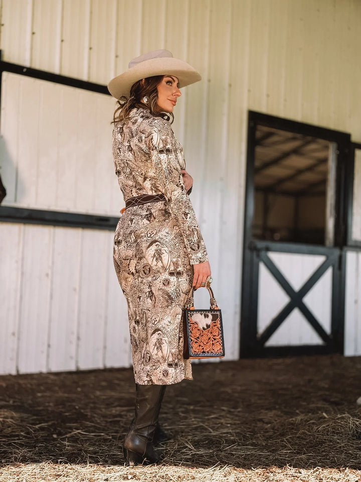 Woman in a paisley western dress, cowboy hat, and boots holding a western handbag outdoors.