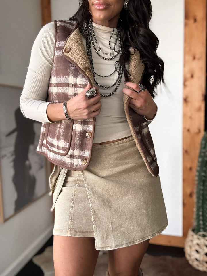 Woman wearing a plaid vest over a white shirt and beige skirt, holding a can.