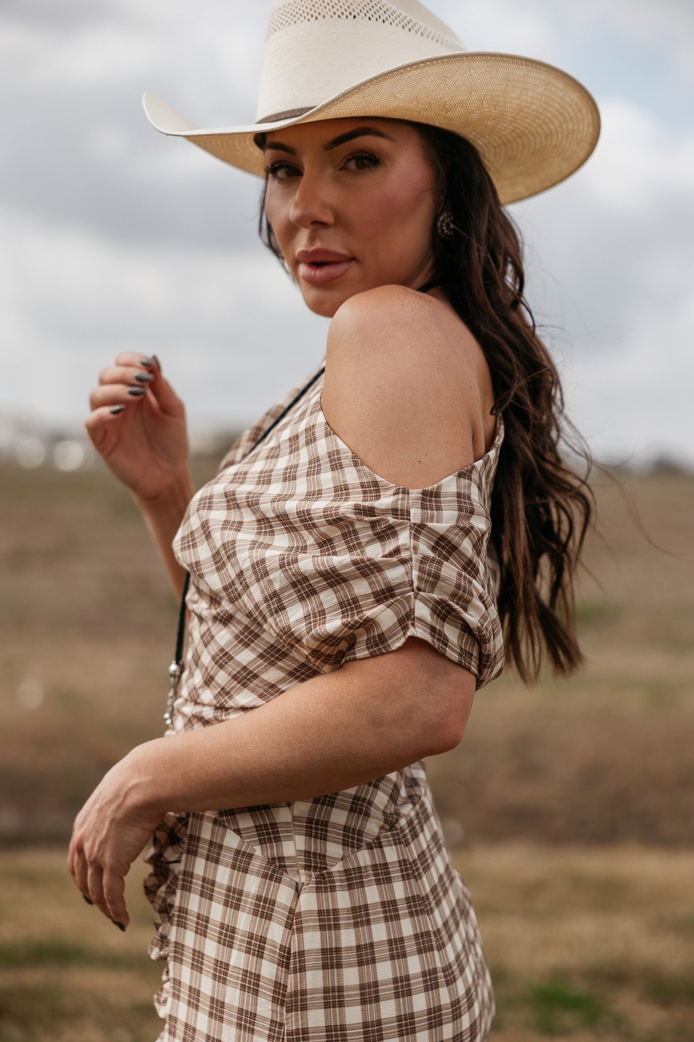Woman in western plaid off-shoulder dress and cowboy hat outdoors, cowgirl boho style