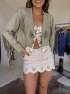 Woman in western fringe jacket, floral crop top, and white eyelet mini skirt, western boho style.