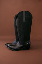 Black leather western cowboy boots with stitched detailing on a brown background