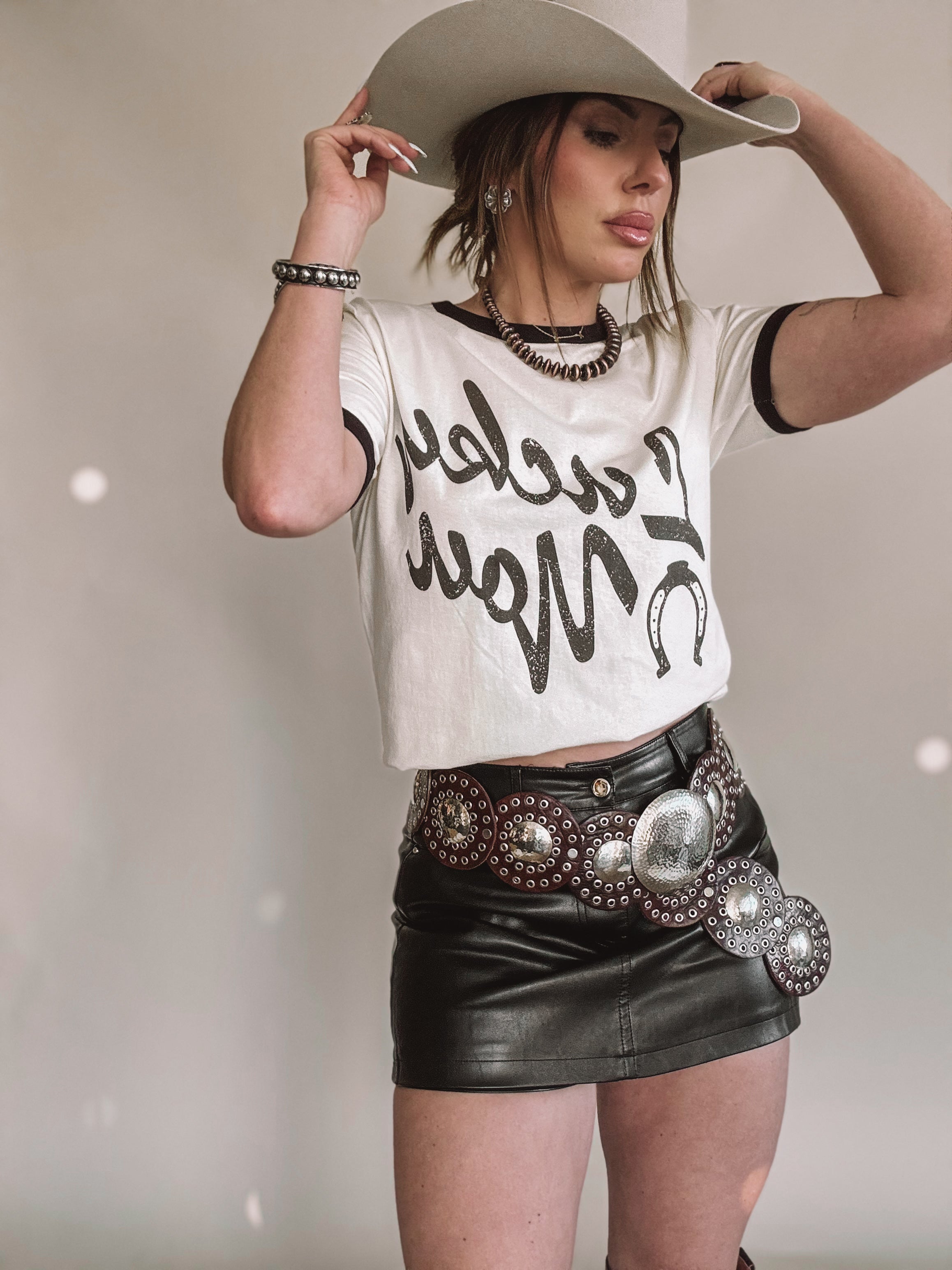 Woman in western boho outfit with cowboy hat, graphic tee, leather mini skirt and concho belt