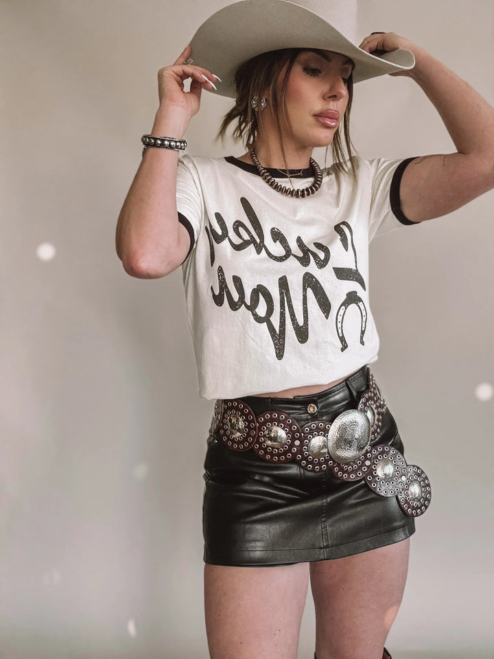 Woman in western boho outfit with cowboy hat, graphic tee, leather mini skirt and concho belt