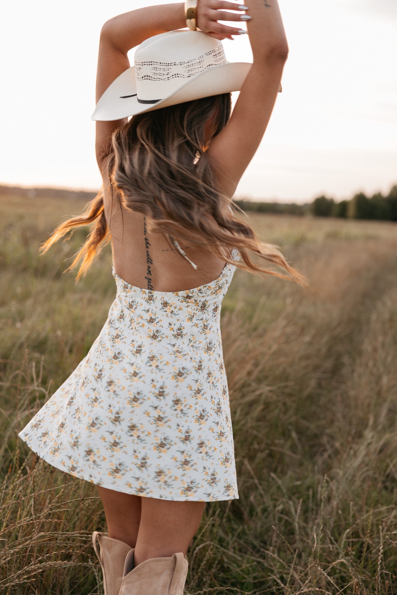 Woman in a floral dress and cowboy hat standing in a field