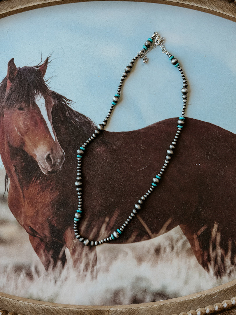 Western beaded necklace with turquoise accents displayed on a horse-themed background