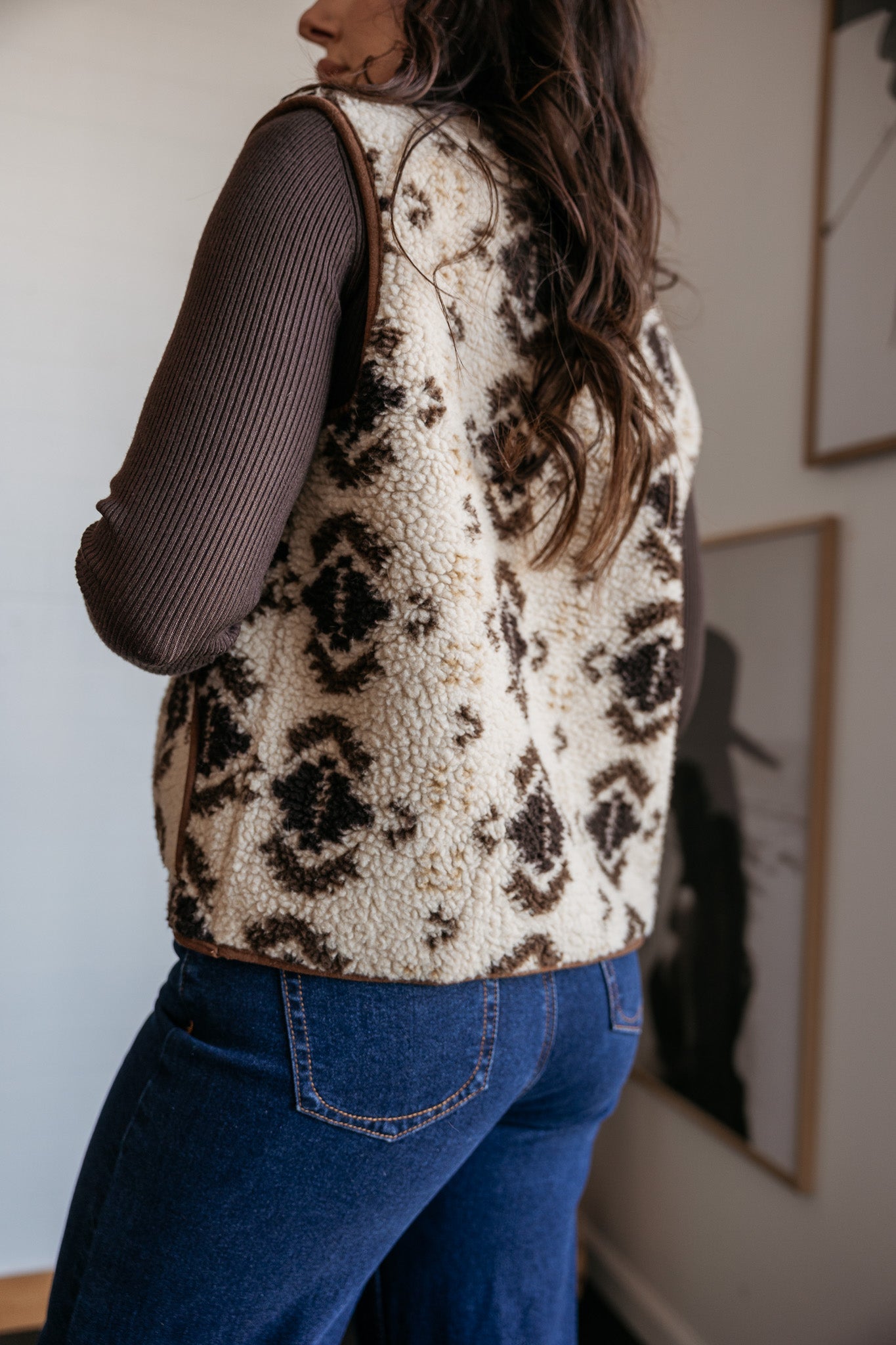 Woman wearing sherpa western print vest, ribbed brown top, and blue jeans